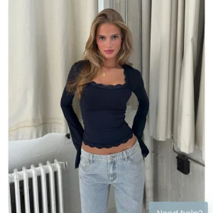 Mörkblå långärmad topp med spets - Snygg mörkblå långärmad topp med tight passform och fyrkantig ringning. Spetsdetaljer vid halsringning och nederkant ger en feminin touch. Perfekt att styla med jeans för en trendig look.