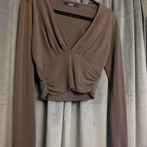 Brun croppad omlottopp från Bik Bok - Säljer en brun croppad topp från Bik Bok i omlottmodell med djup v-ringning och långa ärmar. Toppen har snygga draperingar framtill, Använd mycket fåtal gånger och passar även storlek S!🫶🏻