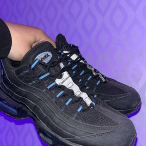 Nike Air Max 95 svart/blå sneakers - Nike Air Max 95 sneakers i svart med blå detaljer. Ovandel i mesh och syntet, ikoniska vågformade paneler och synlig Air Max-dämpning i sulan. Skorna har snörning med blå öglor och en chunky svart yttersula. Perfekta för dig som gillar streetstyle och sportig vibe. Box finns också om man vill få med.