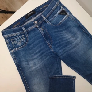 Blå Replay Hyperflex - Snygga blå Replay Hyperflex jeans med skinny fit och klassisk femficksdesign. Jeansen har ljusa slitningar framtill och bak, samt svarta Replay-detaljer på fickorna. Stretchigt material för extra komfort och passform. Modell Anbass, 30:32