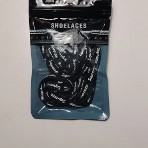 Svarta Supreme skosnören - Säljer ett par svarta skosnören från Supreme med vit logotyp längs hela snöret. Perfekt för att ge dina sneakers en extra touch av streetstyle. Passar de flesta sneakers och är enkla att trä i.