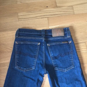 Blå skinny/slim jeans från Nudie - Snygga blå skinny jeans från Nudie med klassisk femficksdesign och kontrastsömmar. Ny pris på jeansen är 1800 kr Jeansen har normalhög midja och är tillverkade i mjukt denimtyg. Perfekta för dig som gillar en tight passform och stilren look.