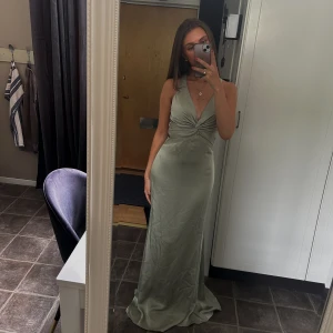 Ljusgrön långklänning med öppen rygg - Supersnygg ljusgrön långklänning i satinliknande material med v-ringning, twistad detalj framtill och öppen rygg med korsade axelband och stor rosett. Aldrig använd då den tyvärr var för lång för mig (är 162 cm). 