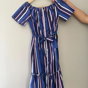 BlåRandig långklänning River Island - Superfin långklänning från River Island med blå, rosa och vita ränder. Klänningen har korta ärmar och silvriga knappar framtill. Perfekt för sommarens alla tillfällen!🌸