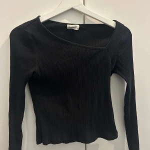 Svart ribbad oneshoulder topp - Snygg svart ribbad topp med lång ärm och asymmetrisk oneshoulder-ringning. Tight passform som framhäver siluetten och ger en trendig look. Perfekt att styla med jeans eller kjol för en cool vibe.