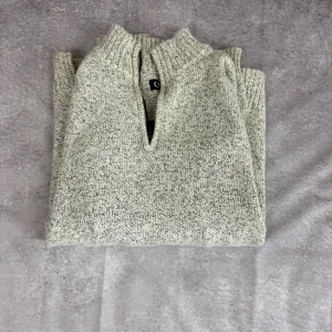 Gråmelerad stickad tröja från Chaps - Snygg gråmelerad stickad tröja från Chaps med halv dragkedja och hög krage. Tröjan har långärmad passform och ribbade muddar vid ärmslut och nederkant. Perfekt för lager-på-lager och chill höst- och vinterstil.