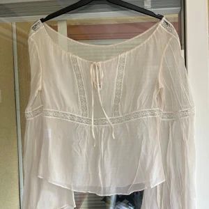 Vit blus med spets och knytband - Superfin vit blus i tunn, luftig siden med broderade spetsdetaljer och knytband framtill. Blusen har långa, vida ärmar. Perfekt för dig som gillar romantisk och bohemisk stil. En mindre skada (se sista bilden). Storlek S . 