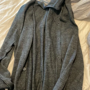 Grå cardigan jacka från 157, M - Mysig grå cardigan jacka från 157 i stickat material. Jackan har knappar framtill och en avslappnad passform med långa ärmar. Perfekt för lager-på-lager och chill dagar.