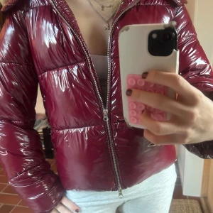 Nelly röd pufferjacka - Säljer en snygg vinröd pufferjacka. Jackan är glansig och har en stor huva, perfekt för kalla dagar. Säljs inte längre och är knappt använd så är helt nyskick. Storlek XS. Skriv vid eventuella frågor!