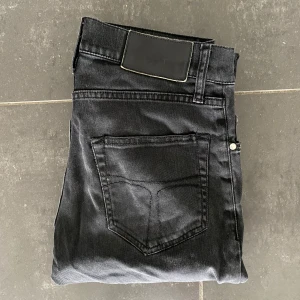 Tiger Of Sweden Jeans - Svarta jeans från Tiger Of Sweden i modellen Pistolero'. De har en klassisk femficksdesign, smal passform och normal midja. Jeansen är tillverkade i ett mjukt bomullstyg med stretch för extra komfort. Perfekta för dig som gillar en stilren och enkel look.