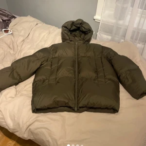 Olivgrön pufferjacka med huva - Säljer en olivgrön pufferjacka med huva och dragkedja framtill. Jackan är quiltad och har en loose passform, perfekt för kalla dagar. Denr helt ny utan prislapp och är en äkta dunjacka därav är priset, skriv för fler bilder 💕