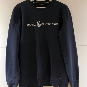 Marinblå Sail Racing sweatshirt - Snygg marinblå sweatshirt från Sail Racing med vit logga tryckt över bröstet. Klassisk rund halsringning och långa ärmar. Perfekt för dig som gillar stilren och sportig look.