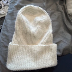 Vit ribbstickad mössa - En stilren vit mössa med bred uppvikt kant och ribbstickad struktur. Perfekt för kalla dagar och enkel att matcha med olika outfits. Mjuk och skön känsla tack vare det stickade materialet.