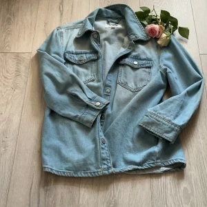 Ljusblå jeansjacka från LAB Industries - Snygg ljusblå jeansskjorta från LAB Industries med klassisk krage, två bröstfickor med knappar och långa ärmar. Skjortan har en avslappnad passform och är tillverkad i mjukt denimtyg. Perfekt att bära öppen eller stängd för en cool look.