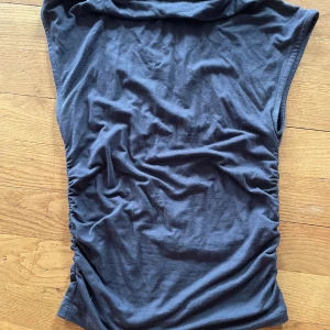 Mörkgrå ärmlös topp från Gina Tricot - Snygg mörkgrå ärmlös topp från Gina Tricot i mjuk bomull. Toppen har rynkade sidor som ger en cool och trendig look. Perfekt att styla med jeans eller kjol för en enkel men stilren outfit.