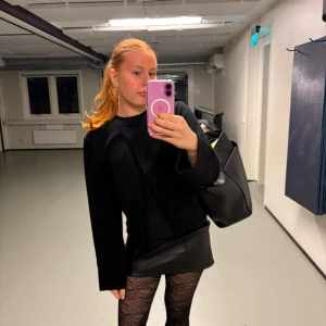 Svart jacka från Gina Tricot - Minimalistisk svart jacka från Gina Tricot med rund halsringning och asymmetrisk knäppning med en knapp. Jackan är croppad och har långa ärmar med breda muddar. Perfekt att styla med kjol eller jeans för en clean look.