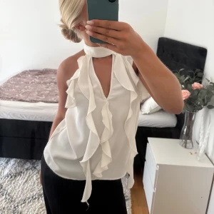 Vit volangblus  - Säljer en vit blus från Zara med hög hals och djup v-ringning både fram och bak. Blusen har volangdetaljer framtill och är ärmlös. Denna har använts några gånger men är fortfarande i fint skick! I strl S 🙌🏼🥰
