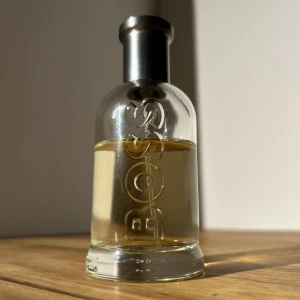 Hugo Boss Bottled Eau de Toilette - Klassisk parfym från Hugo Boss med fräsch doft av äpple, kanel och geranium, samt sensuella tränoter. Flaskan är genomskinlig med BOSS-logga i relief och har en silverfärgad metallkork. Perfekt för dig som gillar eleganta och maskulina dofter.
