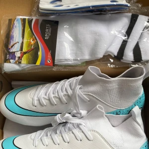 Vita och turkosa fotbollsskor strl 42 - Snygga fotbollsskor i vitt med turkosa och svarta detaljer. Skorna har snörning, hög strumpliknande krage och platt sula med dobbar för bra grepp på planen. Tillverkade i syntetmaterial och designade för att sticka ut på matchen.