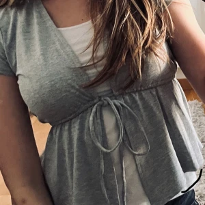 Grå omlottopp med knyt - Supersöt grå omlottopp med knyt i midjan och korta ärmar. Knappt använd 