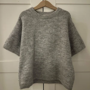 Helt ny Grå stickad tröja från Gina Tricot - Mysig grå stickad tröja från Gina Tricot med korta ärmar och rund halsringning. Tröjan har en loose passform. Enkel och stilren design som funkar till många outfits. Helt ny men bortklippt prislapp! Aldrig använd och inte nopprig💞