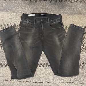Replay Anbass svarta skinny jeans - Svarta Replay Anbass skinny jeans med snyggt tvättad look och klassiska fem fickor. Jeansen har diskreta Replay-loggor, smal passform och stretchigt material för extra komfort. Perfekta för dig som gillar en modern och stilren vibe.Den är lite sliten men inga hål.Ny pris 1200kr