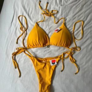 Gul bikini med snörning från Bikbok - Överdelen är i storlek L  Underdelen är i storlek XS Köpte bikini utan att testa då jag ibland har den storleken men passar tyvärr inte. Är helt ny hade någon ”noppra” på sig när jag köpte den. Har guld detaljer längst ut på snörena och mitt emellan kuporna. Är i en orange aktig färg  Hör av dig om du undrar något mer