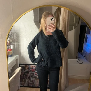 Svart kofta  - Mysig svart kofta från 157 med rund halsringning och knäppning framtill. Koftan är stickad och har en lite fluffig känsla, perfekt att slänga på sig när det är kyligt. Långärmad och i en klassisk, enkel modell som funkar till allt.