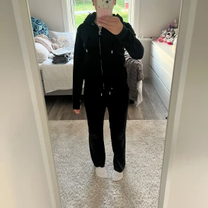 Svart Juicy Couture set  - Svart set med byxor för barn i storlek 12/13 år (152/158) från Juicy Couture. Skulle säga att de är stor i storlek och mer 158 än 152. Jämförde med jeans från Gina Tricot i storlek 158 och de är i princip lika långa. Byxorna är i fint använt skick. Inga hål, noppor eller dylikt.  Svart hoodie från Juicy Couture i storlek XS (dam) motsvarar liknande storlek som passar till byxorna. Fint använt skick, några stenar saknas bak på texten.         