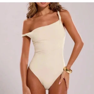 Beige one shoulder body - Snygg beige body med one shoulder-design och twistad axelrem. Stilren och enkel modell som ger en modern vibe. Storlek S