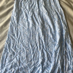 Ljusblå långkjol med blommigt mönster - Söt ljusblå långkjol med vitt blommigt mönster och resår i midjan. Kjolen har en flowy känsla och är perfekt för varma dagar. Materialet känns lätt och luftigt, Vet ej vart den är köpt ifrån *visade att lappen var klippt av* men kommer inte mer till användning. Den är skrynklig men kan stryka innan jag postar den. Kontakta gärna innan köp!