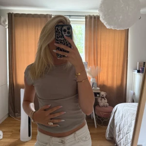 Beige tight topp med kort ärm - Säljer en beige tight topp med korta ärmar och rund hals. Toppens material känns mjukt och stretchigt, perfekt för en avslappnad och trendig look. Passar snyggt till både jeans och kjol. Enkel men stilren design som är lätt att matcha.