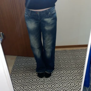 Blå jeans med broderade bakfickor - Säljer ett par blå jeans från Cross med snyggt slitna detaljer och broderade bakfickor. Jeansen har raka ben. De är 40 cm i midjan rakt över och inerbenslängden är 86 cm.