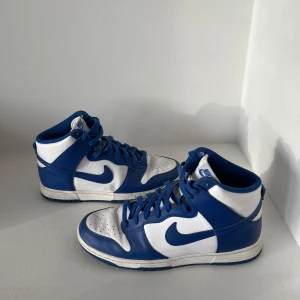 Nike Dunk High blå och vita sneakers - Säljer dessa blåa dunks, har använts lite då och då under två år. Helt okej skick men använda. Köpta för 2750 på soldout, onlinekvitto finns.