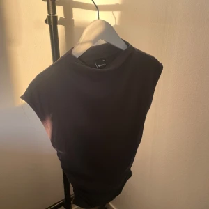 Grå topp som är ribbad och går in på sidorna  - Säljer en mörkgrå, ärmlös topp med rund halsringning. 