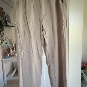 Beiga linnebyxor från 157 - Snygga beiga byxor från 157 i en enkel och stilren design. Byxorna har normal passform, knapp och dragkedja framtill samt hällor för bälte. Perfekta för en avslappnad och clean look.