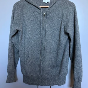 Cashmere hoodie från Davida - Mysig grå stickad hoodie från Davida med dragkedja framtill och två fickor. Tröjan har långa ärmar, huva och ribbade muddar. Perfekt för lager-på-lager och en avslappnad stil.