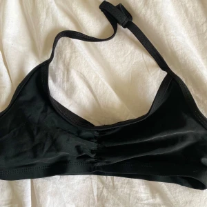 Svart bikiniöverdel med knyt - Säljer en stilren svart bikiniöverdel med enkel axelrem och knyt i nacken. Modellen har en lätt rynkning framtill och är tillverkad i ett mjukt, stretchigt material. Perfekt för strand eller pool!