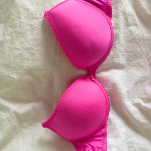 Rosa push-up bh från H&M - Säljer en starkt rosa push-up bh från H&M. Bh:n har släta kupor och inga axelbans. Materialet är mjukt och stretchigt, vilket ger en bekväm passform. Perfekt för dig som vill ha extra lyft och stöd.