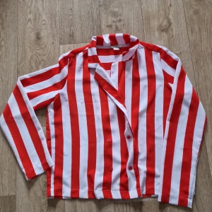 Rödvit randig skjorta/tunn kavaj från Monki - Säljer en skjorta/kavaj från Monki med röda och vita vertikala ränder. Skjortan har lång ärm, knappar framtill och en rak passform. Perfekt för dig som vill sticka ut med ett färgglatt plagg!