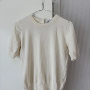 Vit kortärmad tröja från Zara - Säljer en stilren vit kortärmad tröja från Zara. Tröjan har rund halsringning och knappar i ryggen. Den är aningen tajt i ärmarna på mig som vanligtvis bär S/M. Tveka inte på att höra av dig vid frågor eller prisförslag!