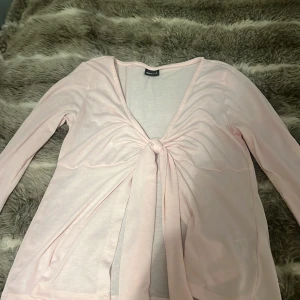 Ljusrosa långärmad topp med knyt från Gina Tricot - Säljer en ljusrosa långärmad topp från Gina Tricot. Toppen har en snygg knytdetalj framtill och är tillverkad i ett tunt, mjukt material. Perfekt att styla med jeans eller kjol för en trendig look. Jättefint på sommaren!