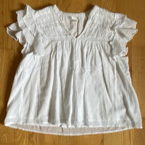 Vit blus med volangärmar från Gina Tricot. - Säljer en luftig vit blus med v-ringning och fina volangdetaljer vid ärmarna. Blusen har en lös  och skön passform och är perfekt för varma dagar. 