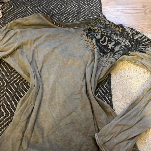 Grå långärmad tröja med tryck från Key Largo - Säljer en grå långärmad tröja från Key Largo med stort svart tryck på ryggen och detaljer framtill. Tröjan har nitar vid halsringningen och texten 'Revolution' på baksidan. Perfekt för dig som gillar unika detaljer och streetstyle.