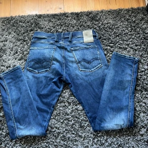Blå Replay Anbass jeans - Säljer ett par blå Replay Anbass Hyperflex jeans med klassisk femficksdesign och snygga slitningar. Jeansen har slim passform och dragkedja i gylfen. Perfekta för dig som gillar stilrena och bekväma jeans med lite stretch. Storlek 31/32, hör av dig vid funderingar eller bud🙌🍾🤝
