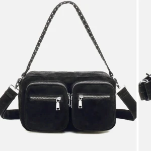 Noella väska  - Snygg svart axelväska i mocka med två stora framfickor och silvriga dragkedjor. Väskan har ett brett axelband med nitar och extra detaljer. Perfekt för dig som vill ha en cool och praktisk accessoar till vardagen.