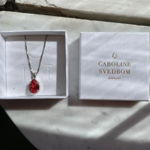 Halsband med rosa Sten från Caroline Svedbom - Säljer ett elegant halsband från Caroline Svedbom med en rosa droppformad sten i silverfärgad kedja. Perfekt för att ge en färgklick till din outfit. Levereras i originalask. Halsbandet är aldrig använt. 