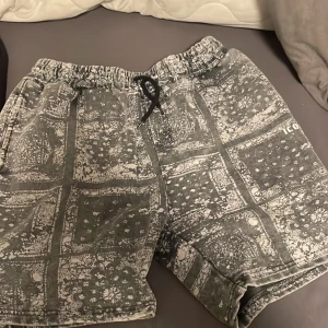 Gråmönstrade shorts med snörning - Säljer ett par grå shorts med vitt mönster och elastisk midja med svart snörning. Shortsen har sidofickor och är jätte sköna