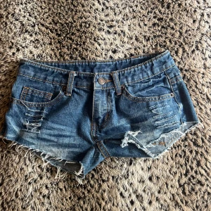 Blå jeansshorts med fransar och slitningar - Snygga blå jeansshorts med slitna detaljer och fransig kant. Klassisk femficksmodell med orange sömmar och låg midja. Perfekta för sommaren och festivaler. Storlek S men väldigt små i storleken så skulle säga XXS/XS