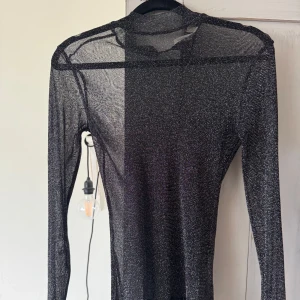 Svart glittrig meshtröja från NLY Trend - Säljer en svart långärmad meshtröja från NLY Trend i storlek XS. Tröjan är glittrig och har en tight passform med genomskinligt material, perfekt för att styla lager på lager. Använd vid 1 nyår 